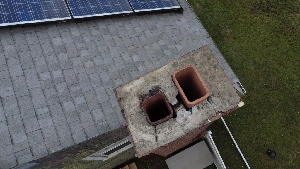 Cracked chimney crown seen from above by drone, with two clay flue tiles exposed