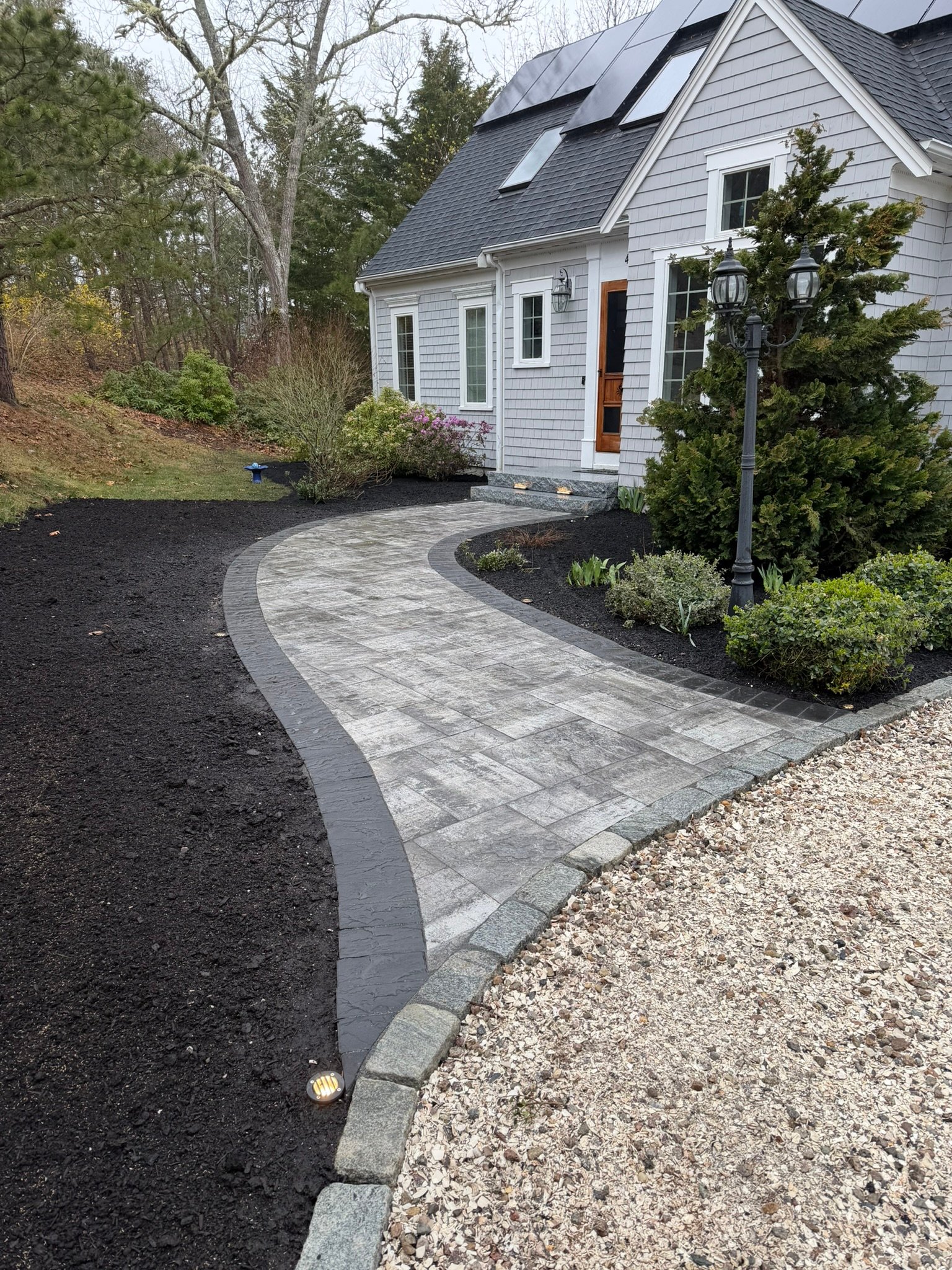 Curved paver walkway with dark border and granite cobblestone edging leading to a front door, Cape Cod MA